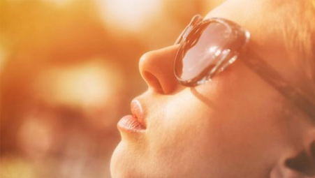 the side view of the face of a young woman in sunglasses basking in the sunshine
